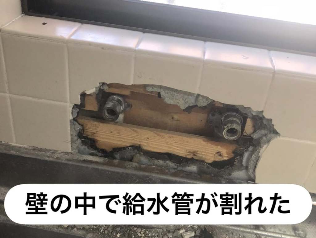 壁に穴が開いており、給水管が割れている状態の画像
