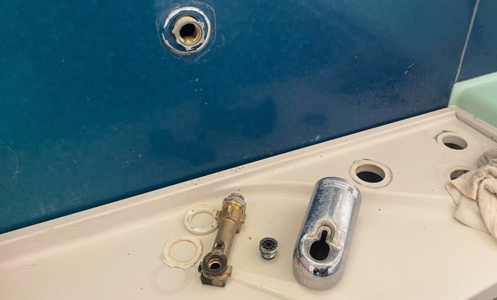 浴室の洗面台にある水道部品と付属品、青い壁と清掃用の布が映っている画像