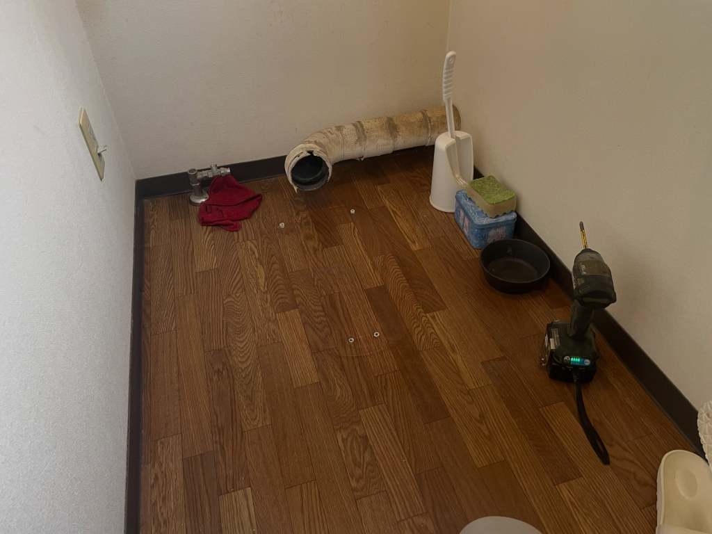 床材が木目調の部屋の一角の写真。左側には電源ソケットがあり、右側にはドリルや容器、タオルなどの道具が置かれている。壁は白く、床はクリーンで整頓されている。